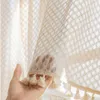 A hand holding a sheer curtain with tassels. Produktbild-Vorschau