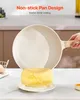 A person is holding a non-stick pan over a cooked omelet on a plate, with kitchen counters in the background. Anteprima dell’immagine prodotto