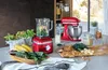 A kitchen counter with a red stand mixer and blender, surrounded by ingredients for making smoothies. Produktbild-Vorschau