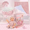A collection of baby doll accessories, including a doll, a bassinet, a pillow, a blanket, and pacifiers, arranged on a pink and white background. Produktbild-Vorschau