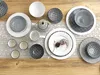 A collection of ceramic tableware, including plates, bowls, cups, and a teapot, arranged on a wooden table with a lace runner. Produktbild-Vorschau