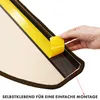 A hand is shown peeling off the protective backing from a strip of double-sided adhesive tape attached to the edge of a carpeted stair tread. Produktbild-Vorschau