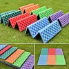 Multiple colorful folding seat cushions are displayed on green grass, with some shown folded and others laid flat. Produktbild-Vorschau