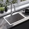 A modern kitchen sink and faucet setup with plants and dishes nearby, set against a window with a view of white flowers. Podgląd zdjęcia produktu