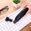 A hand is holding a black USB mini vacuum cleaner over a white keyboard. Glasses and a small potted plant are visible in the background. Voir les images du produit