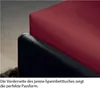 A close-up view of a red fitted sheet draped over a black mattress corner. Produktbild-Vorschau