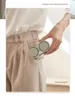 A person's hand is holding a portable neck fan, placing it into the pocket of their beige pants. Náhľad obrázku produktu