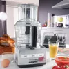 A kitchen scene with a food processor, bread, juice, and tomatoes. Podgląd zdjęcia produktu