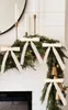A festive Christmas garland decorated with bows and bells, draped over a white paneled wall above a fireplace. Voir les images du produit