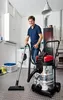 A man is vacuuming in a laundry room with a washing machine and storage cabinets. Produktbild-Vorschau