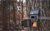 A trail camera is mounted on a tree in a forest. Voir les images du produit