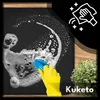 A hand in a yellow glove is cleaning a black mat with a blue scrub brush and soap suds. There is a plant in the background and the brand name 'Kuketo' is visible. Náhled obrázku produktu