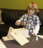 A young boy is assembling a wooden birdhouse kit on a table. Produktbild-Vorschau