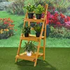 A wooden plant stand with potted plants on it, set in a garden with flowers and grass. Produktbild-Vorschau