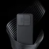 A black phone case with a textured surface and a camera cover is showcased against a dark, abstract background with swirling metallic ribbons. Náhľad obrázku produktu