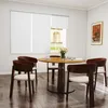 A dining room setting with a round wooden table and chairs, set near a window with white roller blinds. Produktbild-Vorschau