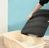 A person is holding a black litter mat over a beige litter box, with litter falling through the mat. Náhled obrázku produktu