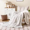 A white faux fur blanket draped over a chair next to a side table with a lamp and decor. Produktbild-Vorschau