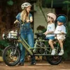 A woman is standing next to an electric cargo bike with two children seated on the back. Produktbild-Vorschau