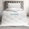 A white quilted duvet and pillows are neatly arranged on a bed with a grey tufted headboard. Produktbild-Vorschau