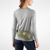 A woman wearing a grey long-sleeved shirt and dark blue pants is shown from the back, wearing a green hip pack around her waist. Voir les images du produit