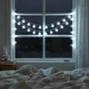 A cozy bedroom scene with snowflake string lights decorating a window at night. Náhled obrázku produktu
