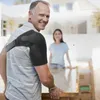 A man wearing a shoulder brace is helping a woman move a large box. Anteprima dell’immagine prodotto