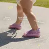 Baby trägt lila und rosa gestrickte erste Lauflernschuhe mit weiter Zehenbox, flexibler Sohle und atmungsaktivem Obermaterial, draußen gehend Anteprima dell’immagine prodotto