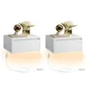 Two white floating nightstands are displayed against a white background. Each nightstand has a drawer and is decorated with a book, a golden orb lamp, and a vase of white flowers. LED lights beneath the nightstands cast an orange glow. Produktbild-Vorschau