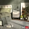 A bedroom scene with a bed, nightstand, plants, and artwork. Produktbild-Vorschau