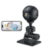 A black mini-WLAN surveillance camera with a stand is shown next to a smartphone displaying a live feed of a woman and a dog in a living room. Produktbild-Vorschau