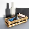 A wooden crate filled with paint cans and a paint roller, with two decorative bottles and a textured black panel in the background. Produktbild-Vorschau