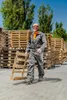 A man in work clothes carries a wooden pallet in front of stacks of pallets. Produktbild-Vorschau
