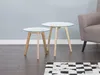 Two round side tables with glass tops and wooden legs are placed on a wooden floor next to a chair. A rug with a black and white checkered pattern is in the foreground. Náhled obrázku produktu