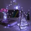 A decorative geometric terrarium filled with fairy lights sits on a table next to a book and a vase of flowers, also illuminated by fairy lights. Podgląd zdjęcia produktu