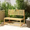 A wooden garden bench is placed on a patio surrounded by lush green plants and foliage, with a glimpse of buildings in the background. Produktbild-Vorschau
