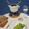 A fondue set is displayed on a table with bread, lettuce, and a glass of white wine. Voir les images du produit