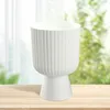 A white planter pot with a ribbed texture sits on a wooden table in front of a blurred background of green foliage and white curtains. Podgląd zdjęcia produktu
