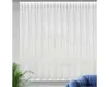 A white sheer curtain hanging in a window, with a plant and a blue chair visible in the foreground. Podgląd zdjęcia produktu