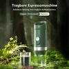 A portable espresso machine is shown in a natural, outdoor setting with greenery and a glass of coffee. Produktbild-Vorschau