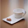 A white coffee cup and saucer with two cookies on a brown surface. Produktbild-Vorschau