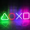 Four neon lights in the shape of PlayStation controller buttons (triangle, circle, cross, square) are displayed in a dark room with a grid-like background and a reflective surface below. Produktbild-Vorschau