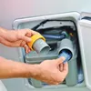 A person is adding a blue tab into a gray container with a yellow ring. Produktbild-Vorschau