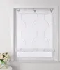 A white window with a beige roller blind with a wavy pattern and small dots. A bouquet of white roses in a teal pot is on a white table to the left. Produktbild-Vorschau