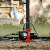 A red and black water pump is set up on the ground, connected to hoses, with a greenhouse or glass structure in the background. Anteprima dell’immagine prodotto