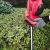 A person wearing a black and white polka dot glove is holding a red electric hedge trimmer, trimming a green hedge. Produktbild-Vorschau
