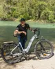 A man stands next to an electric bicycle by a river. Produktbild-Vorschau