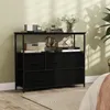 A black fabric dresser with shelves is shown in a bedroom setting, next to a bed. Decorative items are on the top shelf. Anteprima dell’immagine prodotto