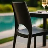 A black chair sits on a patio next to a swimming pool, with a table and glasses in the background. Voir les images du produit