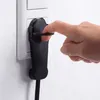 A finger is shown plugging a black electrical plug into a white wall socket. Produktbild-Vorschau